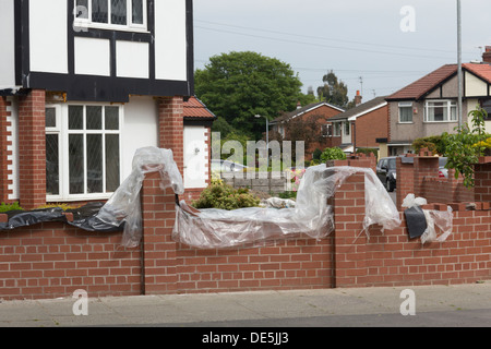 Mur de jardin en construction en brique, couvert par des bâches en plastique à tandis que le mortier sèche sur Bradford Road, Bolton, Lancashire Banque D'Images