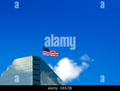 American / USA flag flying au sommet d'un gratte-ciel de verre. Ciel bleu avec un nuage blanc en vue. Banque D'Images