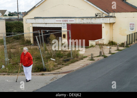 Jaywick, Essex. Retraité senior utilisant un bâton de marche, debout à côté d'une arcade d'amusement, Sunspot Amusements, panneau indiquant Open All Day for Food & Drink sur le domaine de Brooklands. Jaywick est un petit village, niché entre Clacton-on-Sea et les marais et dunes de Colne point. Construit dans les années 1930 comme un village de vacances de chalets pour East Enders de Londres, il a maintenant une population toute l'année et est considéré comme l'une des communautés les plus défavorisées en Grande-Bretagne 2013 2010s UK HOMER SYKES Banque D'Images