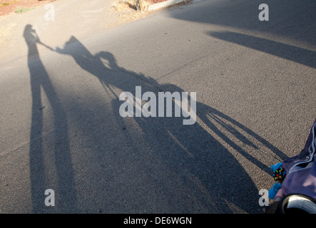 Silhouette d'ombre d'une mère poussant un bébé dans la poussette au coucher du soleil. Banque D'Images