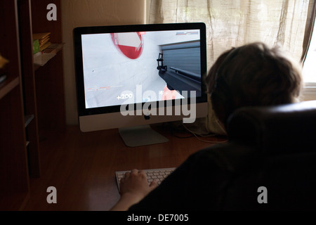 Teenage boy joue en ligne jeu vidéo, Team Fortress 2, à la maison sur ordinateur tout en interagissant avec les autres joueurs via Skype Banque D'Images