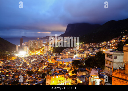 Vue de nuit du haut de la Favela da Rocinha, classe supérieure en arrière-plan de quartier São Conrado, Rio de Janeiro, Brésil. Banque D'Images