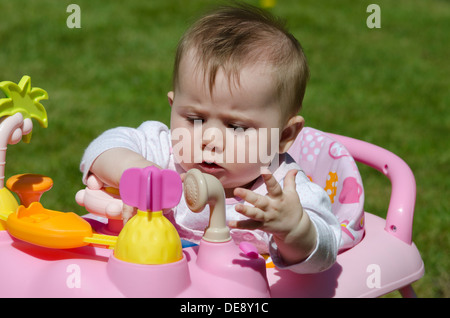 Huit mois bébé fille assis dans une chaise haute avec des jouets dans le jardin pelouse Banque D'Images