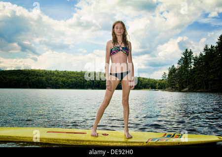 Teen girl debout sur un paddle board flottant dans le lac Banque D'Images