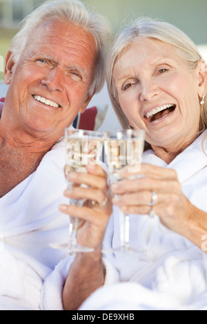 Happy senior homme femme couple en dehors de soleil portant des peignoirs blancs célébrant drinking white wine Champagne Banque D'Images