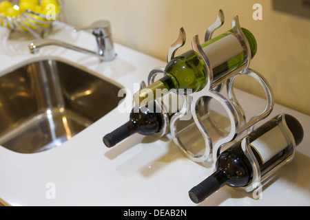 Trois bouteilles de vin avec des étiquettes vierges dans un élégant support de vin sur un comptoir de bar ou de cuisine aux côtés d'un lavabo Banque D'Images