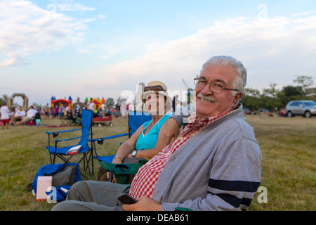 Vieux couple de spectateurs assis dans des transats lors d'une activité de plein air dans un champ tournant de sourire à l'appareil photo Banque D'Images