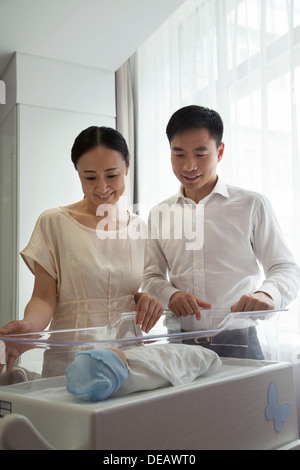 Jeune famille heureuse en regardant leur nouveau-né dans la crèche de l'hôpital Banque D'Images