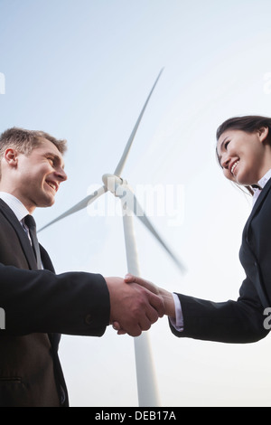 Deux smiling young business people shaking hands en face d'une éolienne Banque D'Images