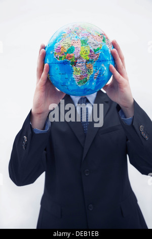 Businessman in a suit holding a globe jusqu'en face de son visage, visage masqué, studio shot Banque D'Images