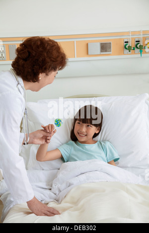 Femme médecin de donner une sucette à une jeune fille couchée dans un lit d'hôpital Banque D'Images