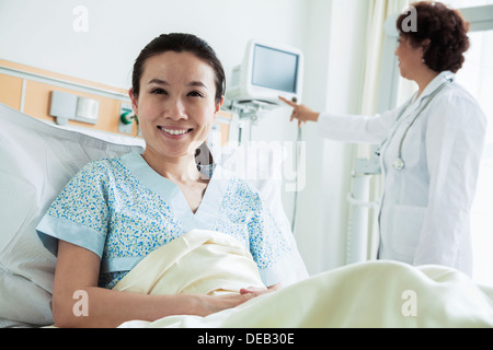 Female patient assis dans un lit d'hôpital, médecin à l'aide de matériel médical dans l'arrière-plan Banque D'Images