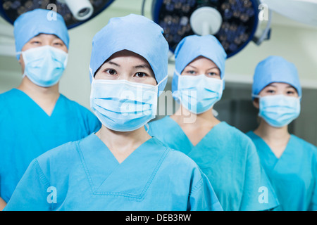 Équipe de chirurgiens portant des masques chirurgicaux dans la salle d'opération, looking at camera Banque D'Images