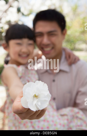 Fille tenant une fleur de cerisier près de l'appareil photo avec son père dans le parc au printemps Banque D'Images