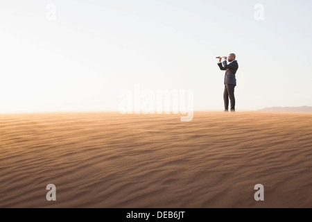 Young businessman looking through telescope au milieu du désert Banque D'Images