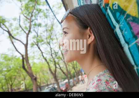 Vue latérale du jeune femme avec des lunettes appuyé contre un mur recouvert de graffitis Banque D'Images