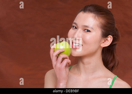 Jeune femme tenant une pomme et se préparer à prendre une bouchée, looking at camera, studio shot Banque D'Images