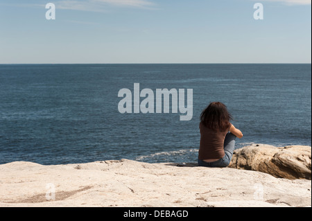 Une jeune femme assise seule sur le les falaises de Point Judith, Rhode Island USA donnant sur l'océan. Banque D'Images