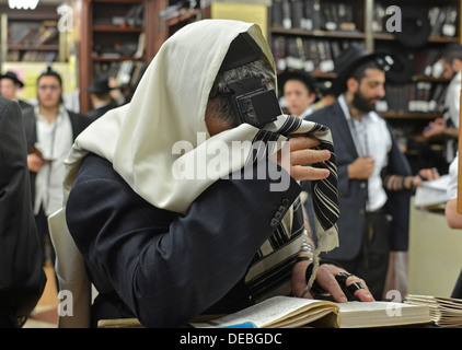 Un homme juif religieux en prière lors d'une synagogue de Brooklyn, New York. Ses yeux sont couverts d'une partie de l'office du matin. Banque D'Images