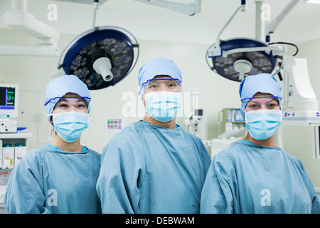 Portrait de trois chirurgiens dans une ligne portant des masques chirurgicaux dans la salle d'opération, looking at camera Banque D'Images