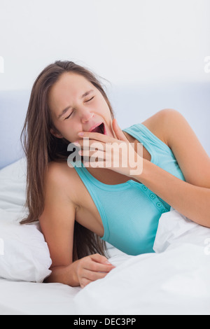 Tired woman yawning sitting on her bed