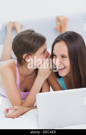 Happy girls lying in bed with laptop Banque D'Images