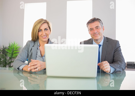 Deux smiling business people looking at camera derrière un ordinateur portable Banque D'Images