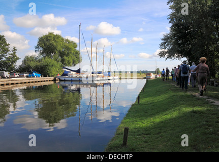 Une vue de yachts amarrés à Upton Staithe , Norfolk, Angleterre, Royaume-Uni, avec un groupe de randonneurs sur un pays de marche. Banque D'Images