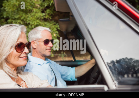 Side view of mature couple driving red cabriolet Banque D'Images