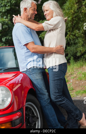 Happy mature couple hugging against their red cabriolet Banque D'Images