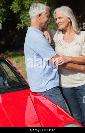 Cheerful mature couple hugging against their red cabriolet Banque D'Images