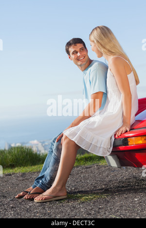 Smiling couple assis sur leur capot de voiture cabriolet Banque D'Images