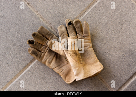 Gants de travail en cuir usé allongé sur un patio en béton. Banque D'Images