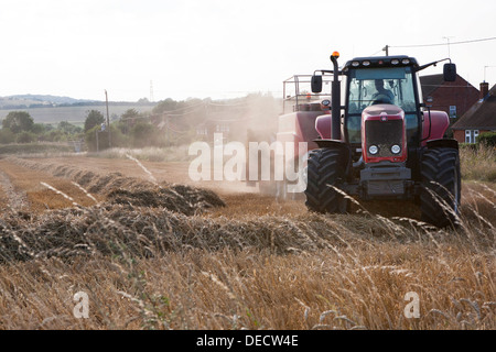 Un tracteur Massey Ferguson rouge et la ramasseuse-presse pressage de paille en pleine campagne. Banque D'Images