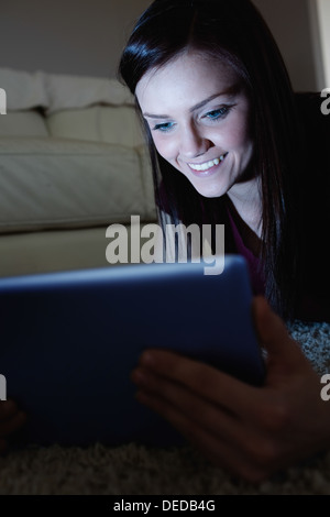 Smiling brunette lying on floor using tablet pc dans le noir Banque D'Images