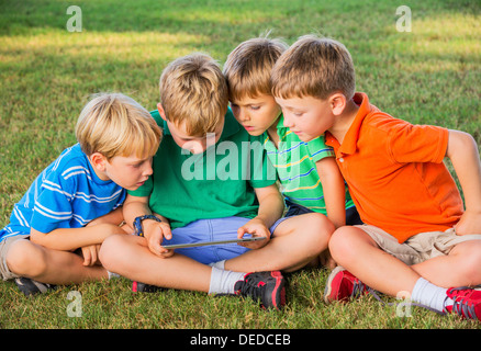 Groupe d'enfants assis sur l'herbe et using tablet computer Banque D'Images