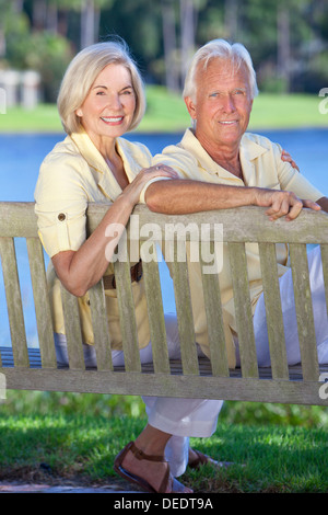 Happy senior couple assis sur un banc de parc à côté d'un lac bleu Banque D'Images