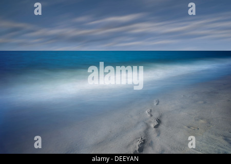 Des empreintes de pas dans le sable et flous, les vagues de l'océan avec nuages en mouvement Banque D'Images