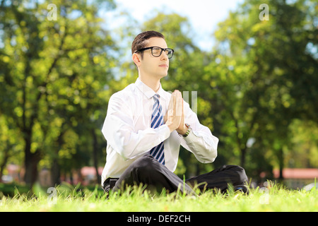 Jeune homme avec des lunettes faisant du yoga exercice assis sur une pelouse dans un parc Banque D'Images