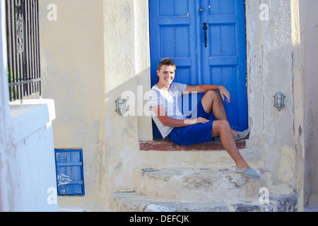Jeune homme assis près de l'ancienne porte bleue d'Emporio village sur l'île Santorin, Grèce Banque D'Images