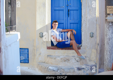 Jeune homme assis près de l'ancienne porte bleue d'Emporio village sur l'île Santorin, Grèce Banque D'Images