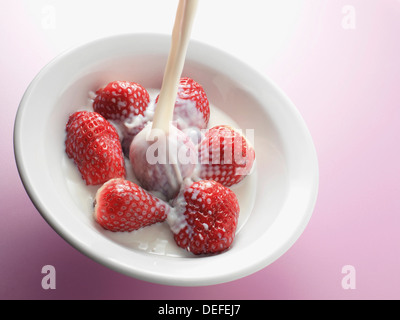Le lait frais est versé sur un bol de fraises Banque D'Images