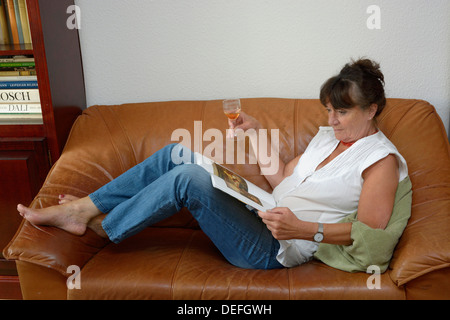 Femme, milieu des années 60, de boire un verre de vin lors de la lecture Banque D'Images