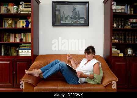 Femme, milieu des années 60, de boire un verre de vin lors de la lecture Banque D'Images