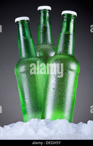 Trois bouteilles de bière verte assise sur la glace sur un fond gris. Banque D'Images