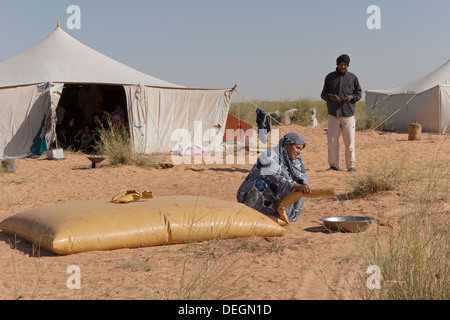 Femme de la famille nomade, portant la robe traditionnelle mauritanienne, mulafa, prenant l'eau de la vessie de stockage dans la région de desert Banque D'Images