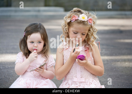 Deux filles préadolescentes portant des robes roses et de mettre du rouge à lèvres. Banque D'Images