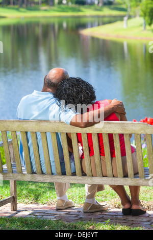 Vue arrière d'un happy senior African American couple assis sur un banc de parc à faire place au à un lac ou rivière Banque D'Images