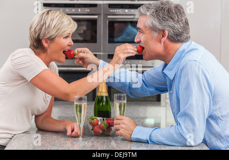 Un joli sourire, heureux, l'homme et de la femme romantique couple Fraises et champagne dans une cuisine Banque D'Images