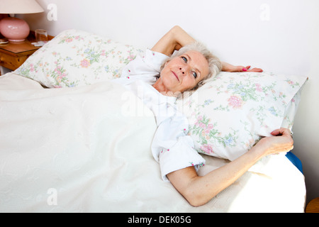 High angle view senior woman looking away while lying bed accueil Banque D'Images